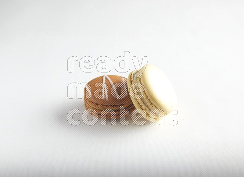 45º Shot of of two assorted Brown Irish Cream, and Yellow Vanilla macarons on white background