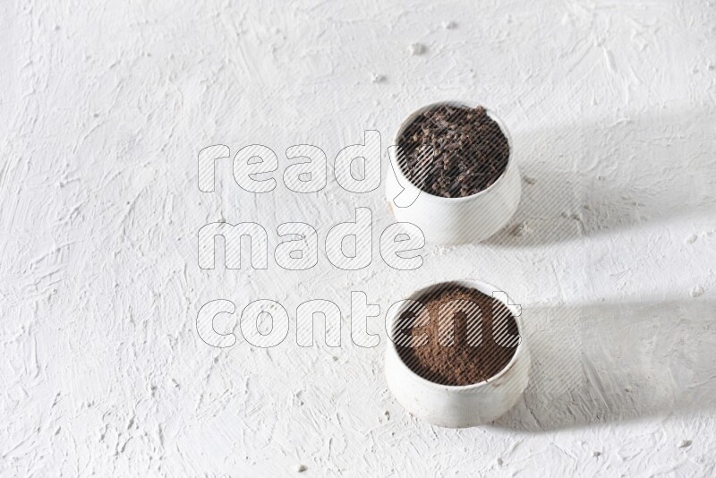2 Beige ceramic bowls, one full of cloves and the other full of powder on textured white flooring