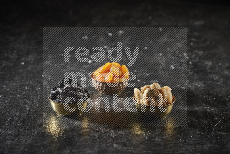 Dried fruits in metal bowls in a dark setup