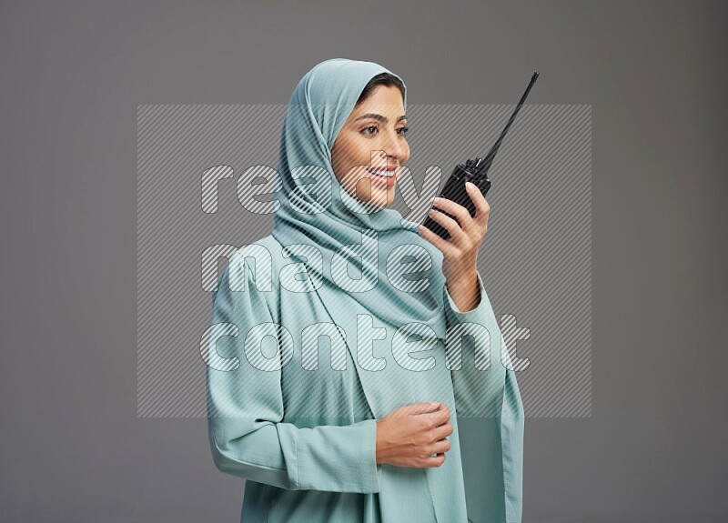 Saudi Woman wearing Abaya standing holding walkie-talkie on Gray background