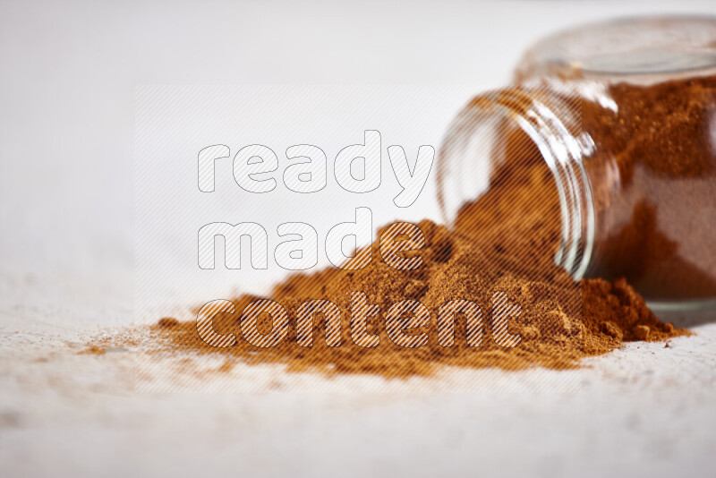 A glass jar full of ground paprika powder flipped with some spilling powder on white background