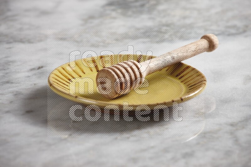 Multicolored pottery plate with wooden honey dipper in it on grey marble background