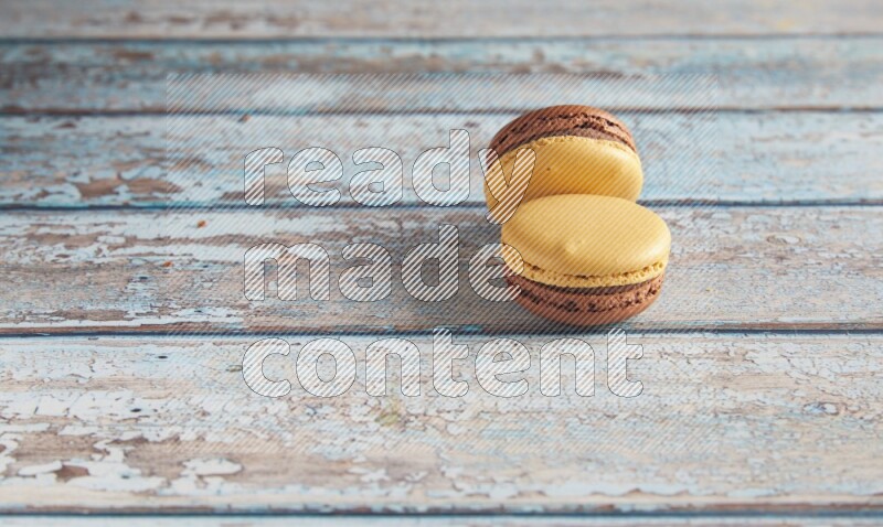 45º Shot of two Yellow and Brown Chai Latte macarons on light blue wooden background