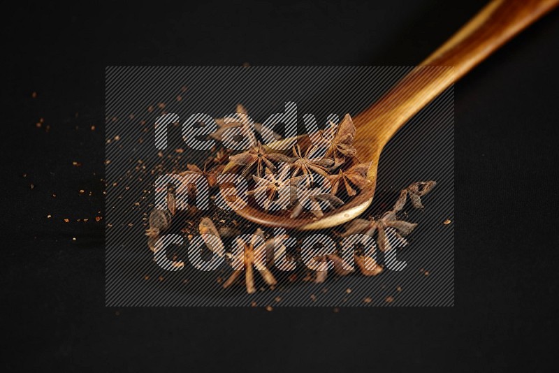 Star Anise in a wooden spoon ladle with more anise on black flooring