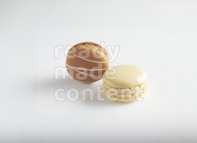 45º Shot of of two assorted Brown Irish Cream, and Yellow Vanilla macarons on white background