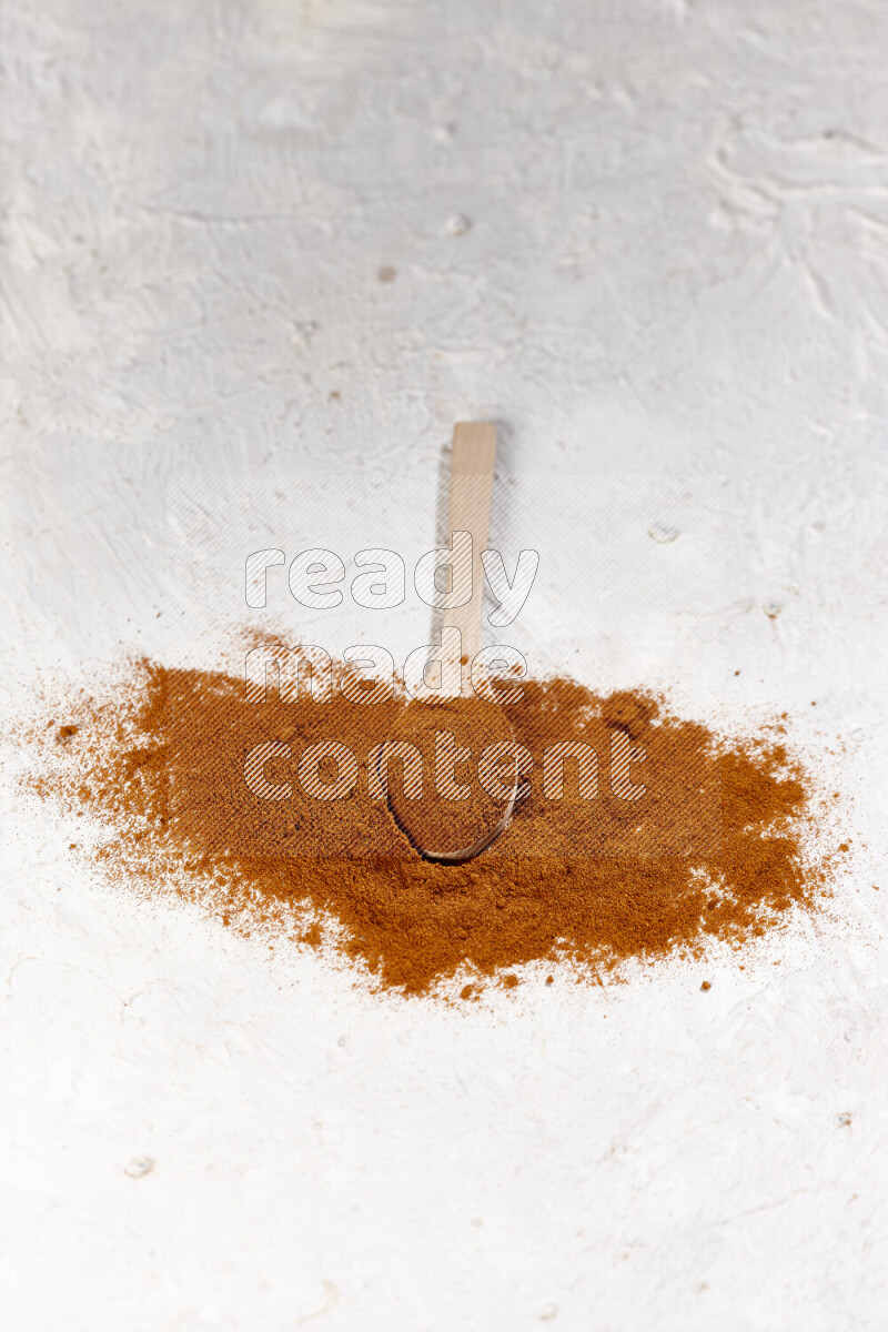 A wooden spoon full of ground paprika powder and surrounded with the powder on white background