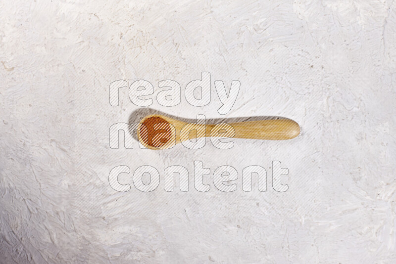 A wooden spoon full of ground paprika powder on white background