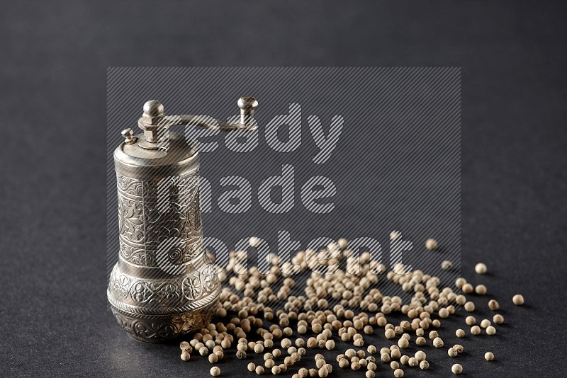 White pepper with a metal pepper grinder on black flooring