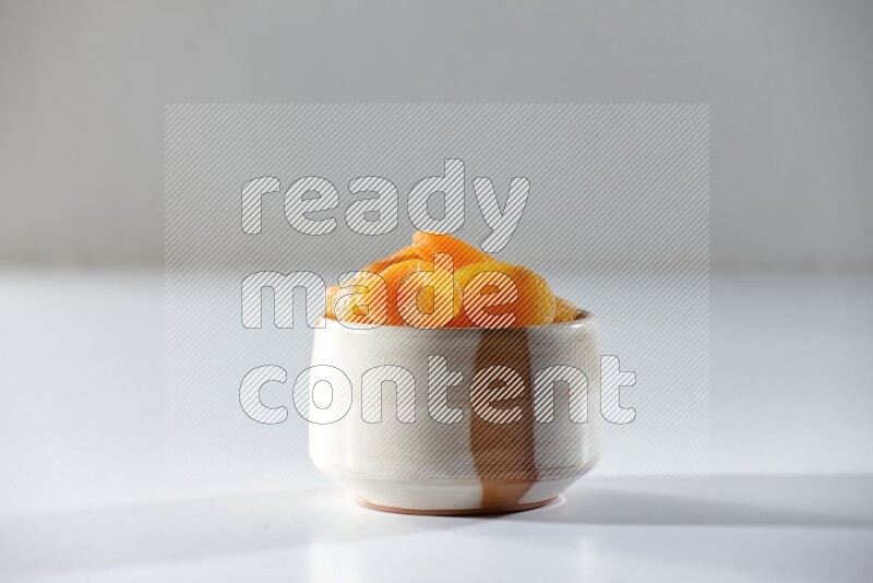 A beige ceramic bowl full of dried apricots on a white background in different angles