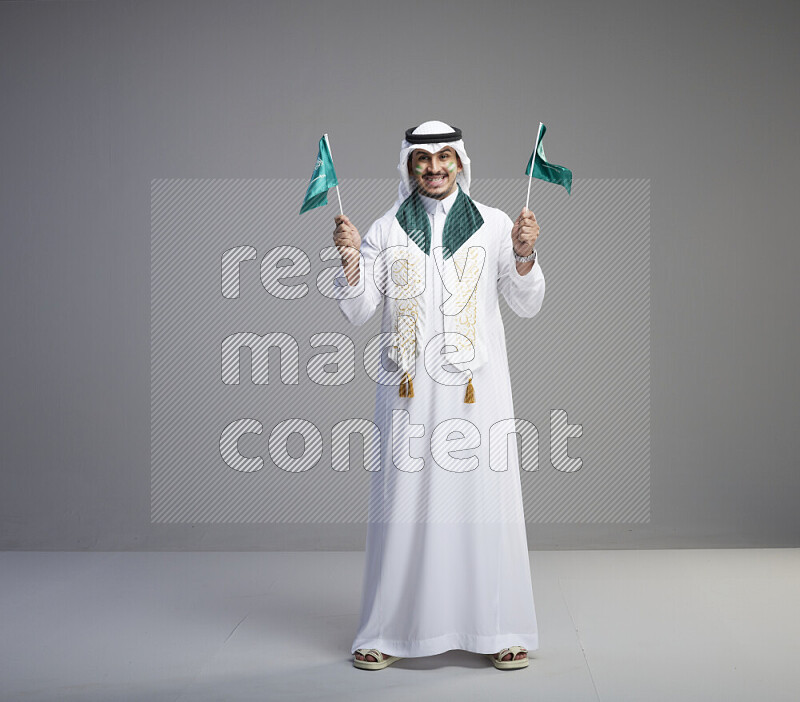 رجل سعودي يرتدي ثوب وشماغ ويحمل اعلام السعودية