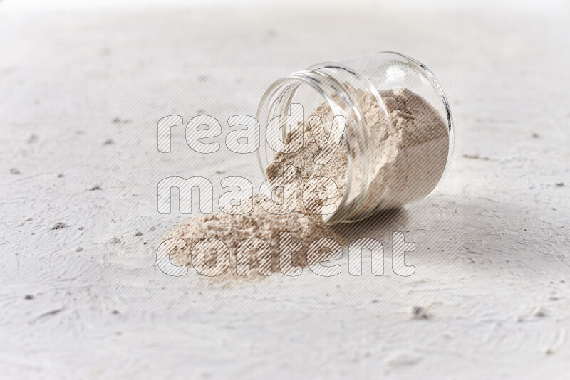 A glass jar full of onion powder flipped with some spilling powder on white background