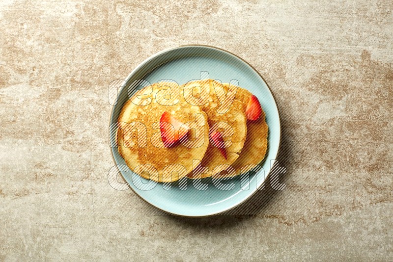 Three stacked strawberry pancakes in a blue plate on beige background