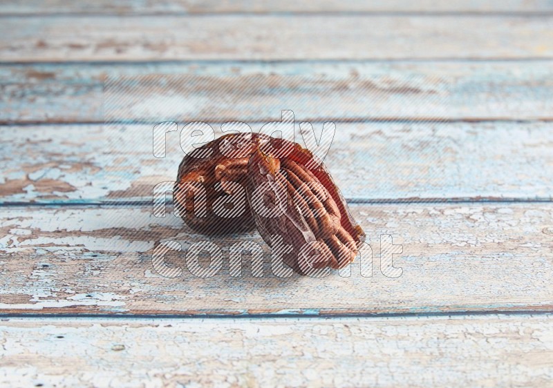 two pecan stuffed madjoul dates on a light blue wooden background