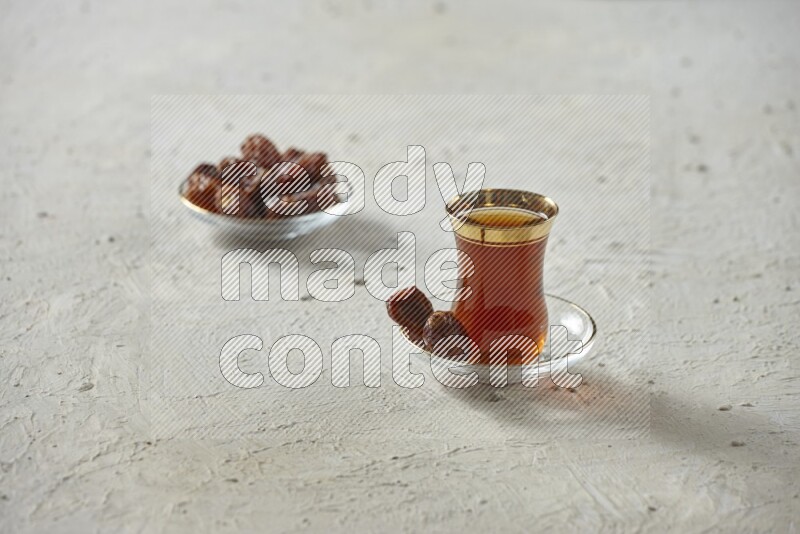 A tea glass cup with dates and coffee on textured white background