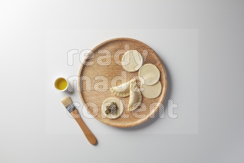two closed sambosas and one open sambosa filled with meat while oil with oil brush aside in a wooden dish on a white background