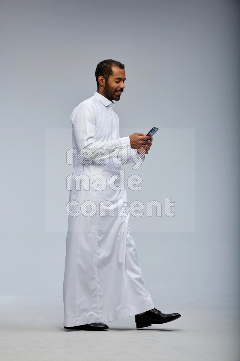 Saudi man wearing Thob standing texting on phone on Gray background