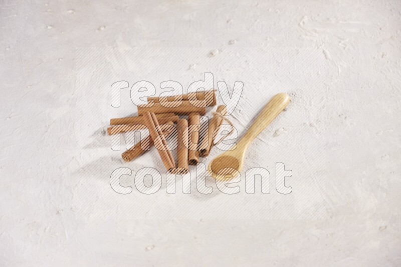 Cinnamon sticks stacked beside a wooden spoon full of cinnamon powder on white background