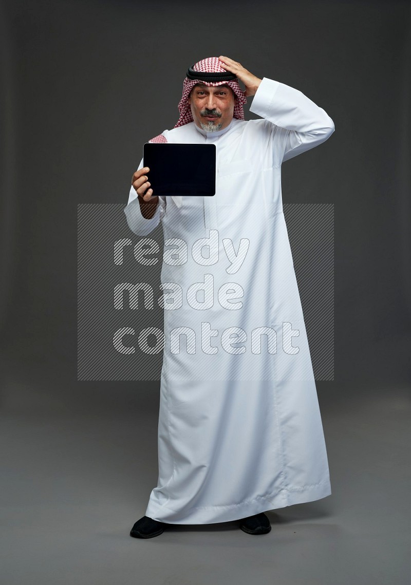 Saudi man with shomag Standing working on tablet on gray background