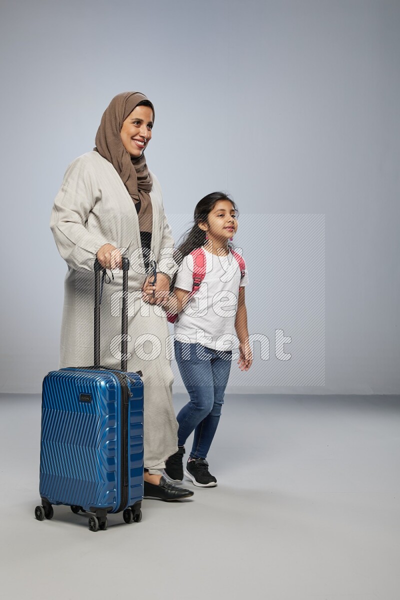 Mom and daughter standing pulling a carry-on bag on gray background