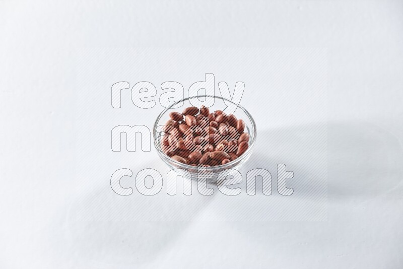 A glass bowl full of red skin peanuts on a white background in different angles