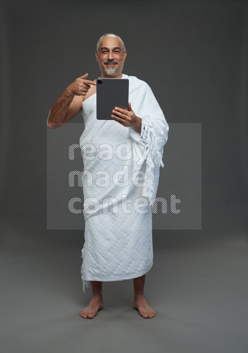 A man wearing Ehram Standing working on tablet on gray background