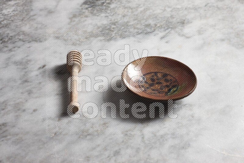Decorative pottery plate with wooden honey dipper on the side on grey marble background