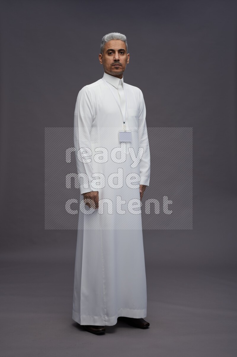 Saudi man wearing thob with neck strap employee badge standing interacting with the camera on gray background