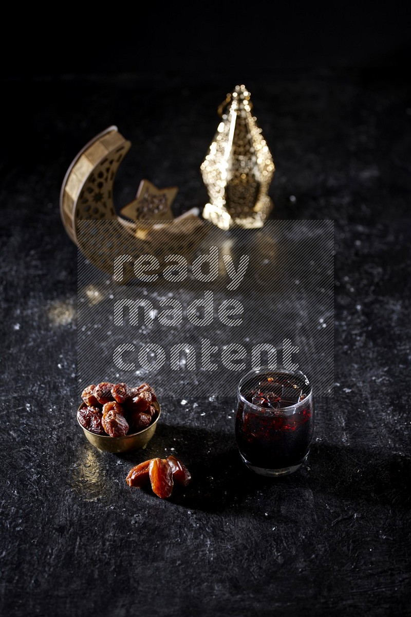 Dates in a metal bowl and tamarand beside a gold crescent and a lantern in a dark setup