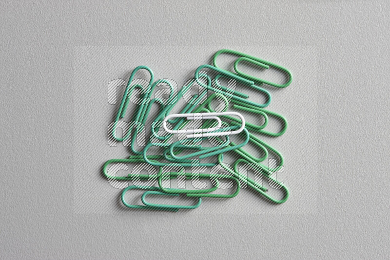 A white paperclip surrounded by bunch of green paperclips on grey background