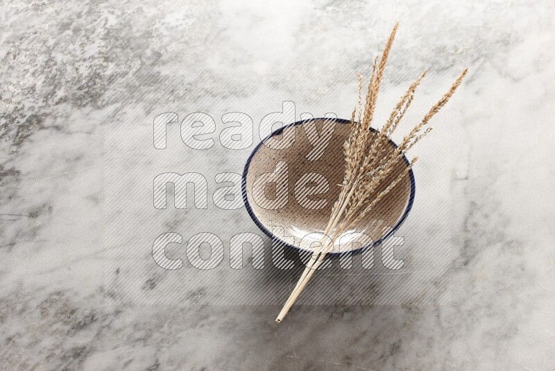 Wheat stalks on multicolored pottery bowl on grey marble background