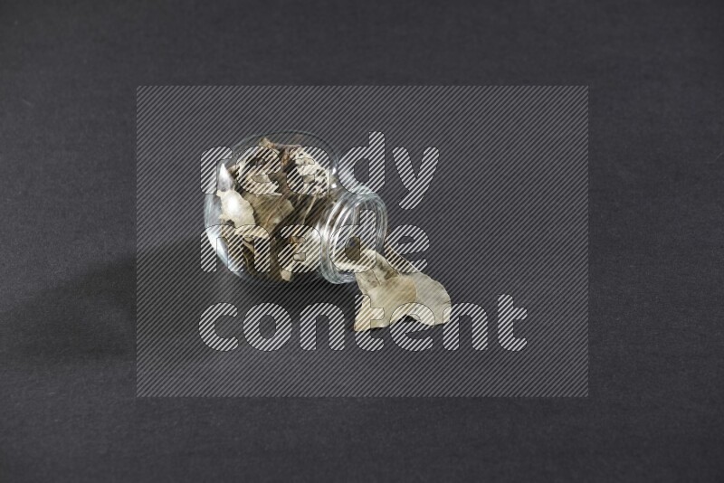 A glass spice jar full of dried bay leaves and jar is flipped and leaves spread out on black flooring