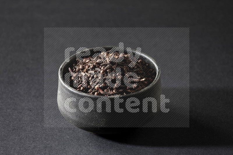 A black pottery bowl full of cloves on a black flooring