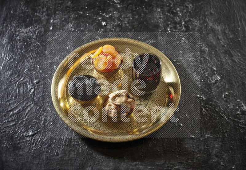 Dried fruits in metal bowls with tamarind on a tray in dark setup