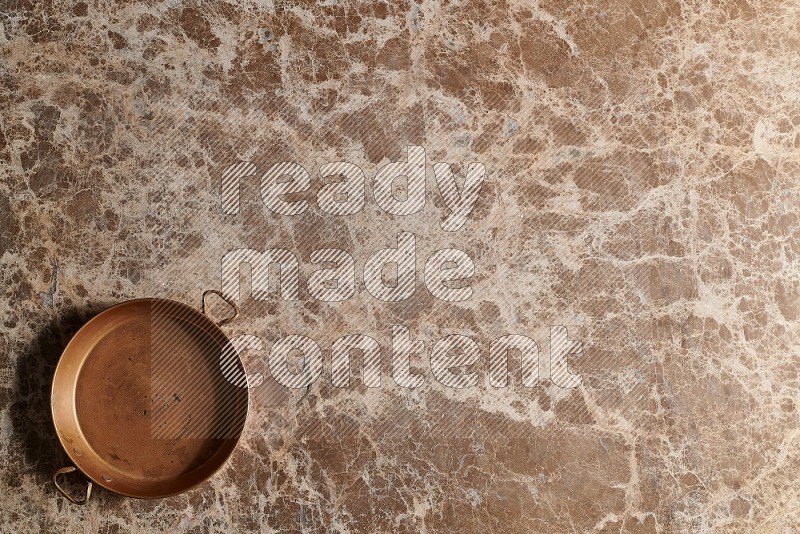 Top View Shot Of A Small Copper pan On beige Marble Flooring
