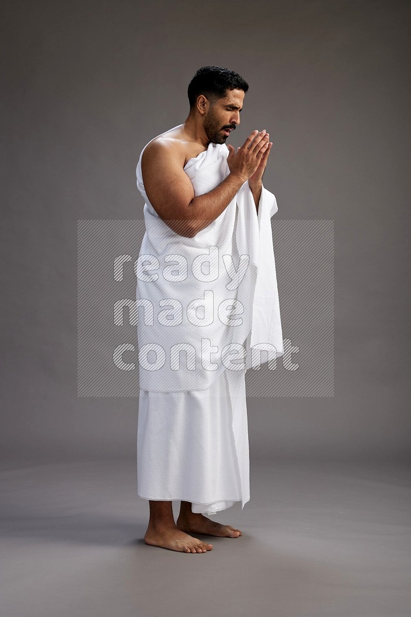 A man wearing Ehram standing showing how to sneeze on gray background