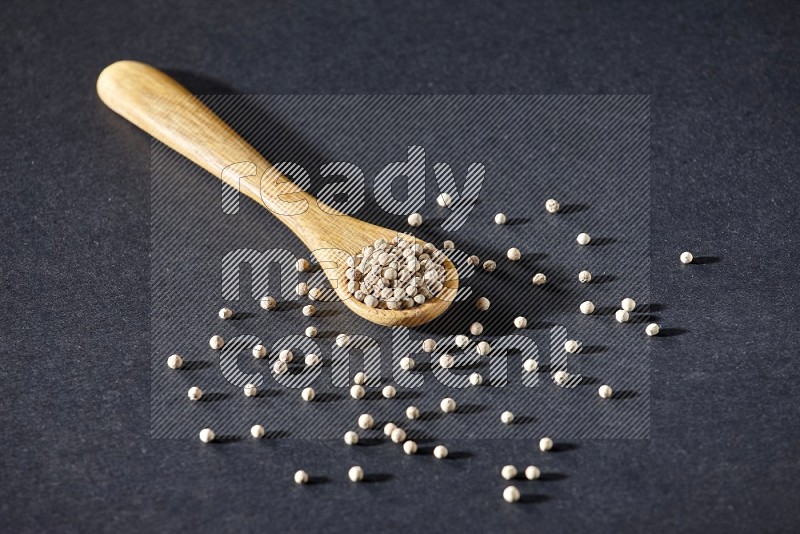 A wooden spoon full of white pepper beads on black flooring