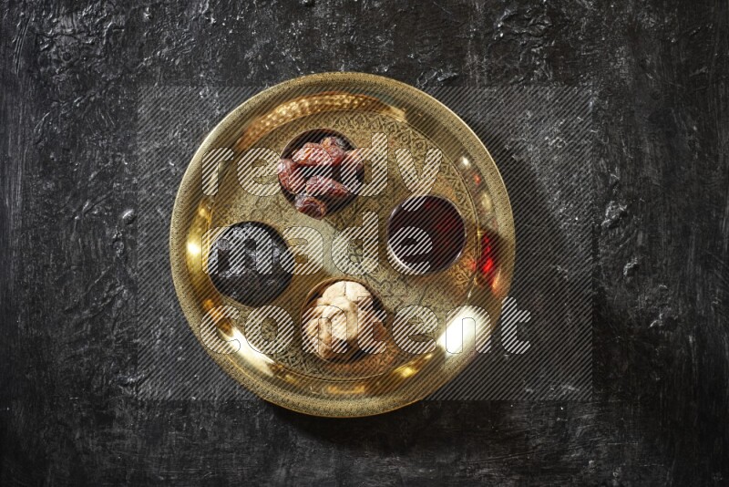 Dried fruits in metal bowls with tamarind on a tray in dark setup