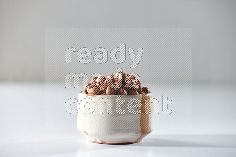 A beige ceramic bowl full of peeled hazelnuts on a white background in different angles