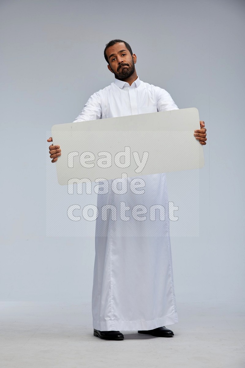 Saudi man wearing Thob standing holding board on Gray background