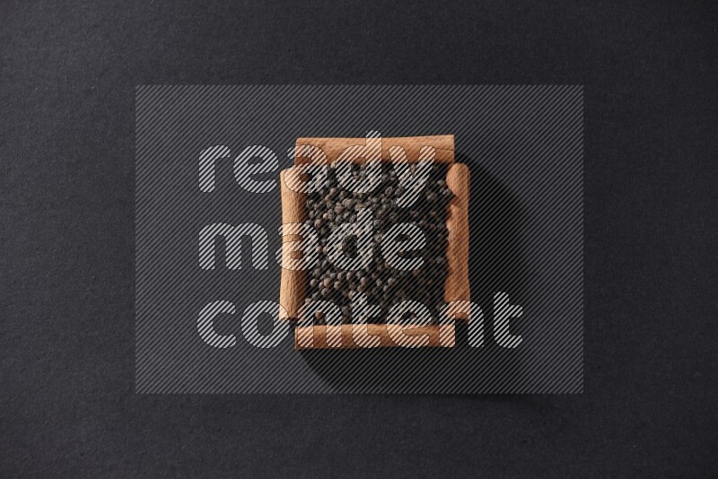 A single square of cinnamon sticks full of black pepper on black flooring