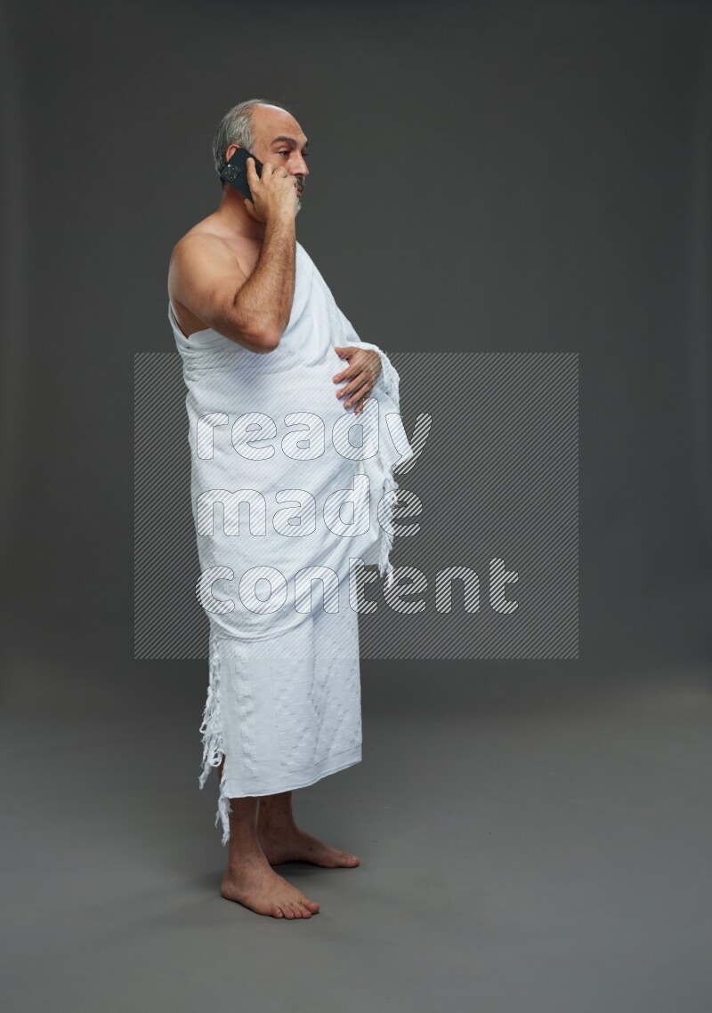 A man wearing Ehram Standing talking on phone on gray background