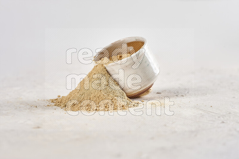 A beige pottery bowl full of ground ginger powder with fallen powder from it on white background