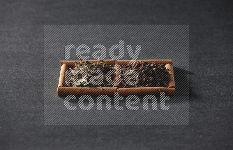 مربعان من أعواد القرفة ممتلئان بالقرنفل والريحان المجفف علي خلفية سوداء