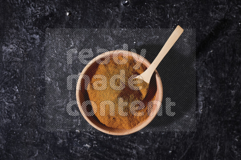 A wooden bowl full of ground paprika powder and a wooden spoon in it on black background