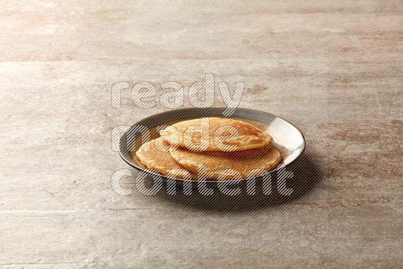 Three stacked plain pancakes in a bicolor plate on beige background