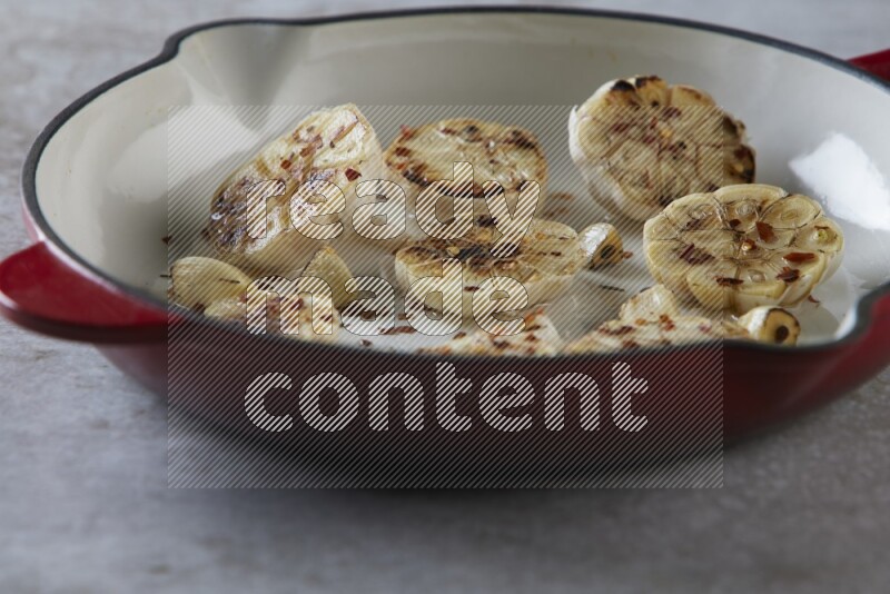 half's roasted garlic in a red-coated cast iron pan on a grey textured countertop
