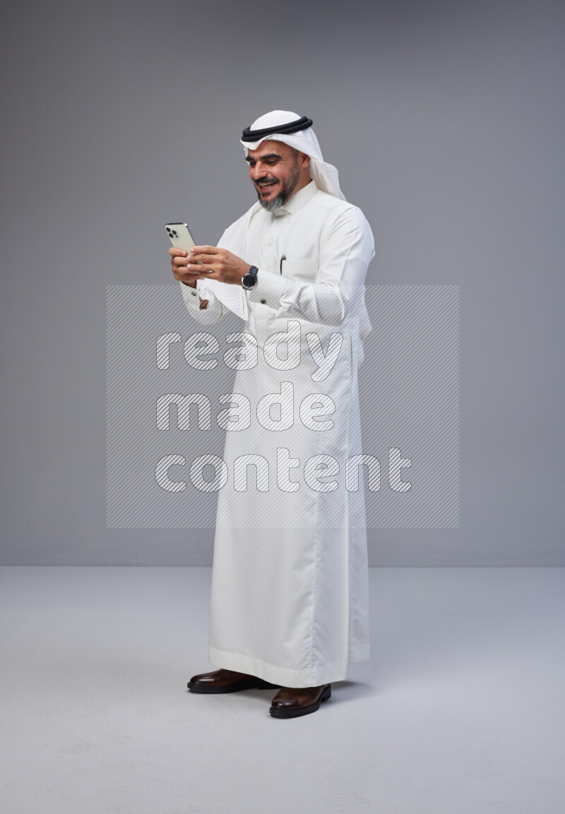 رجل سعودي يرتدي ثوب وشماغ ابيض يحمل هاتف جوال