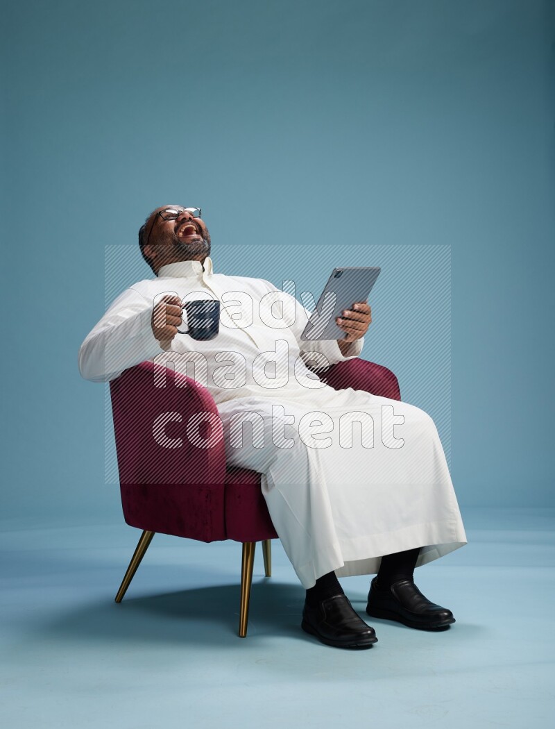 Saudi Man without shimag sitting on chair working on tablet on blue background