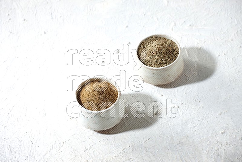 2 beige bowls full of cumin seeds and powder on a textured white flooring