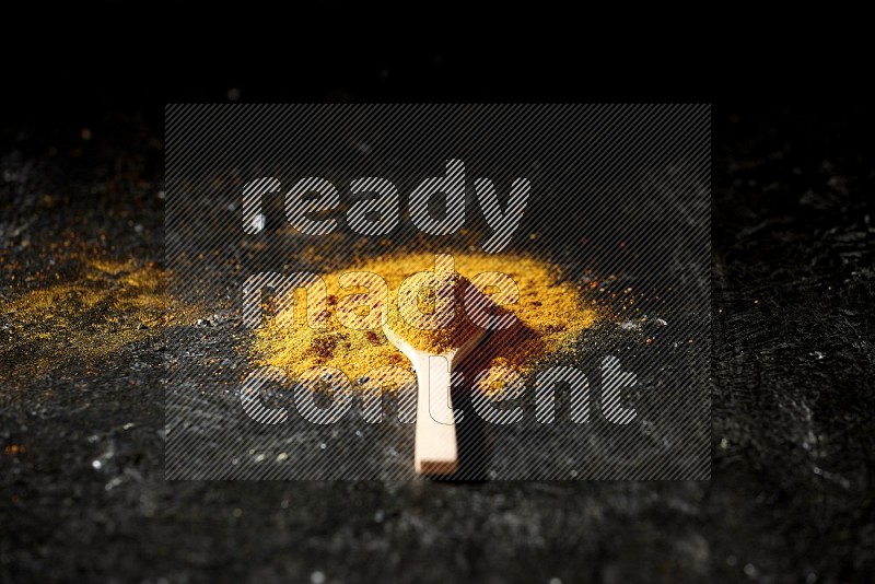 A wooden spoon full of turmeric powder on textured black background